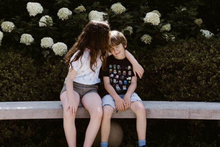 two toddler girl and boy sitting on concrete bench near outdoor during daytime